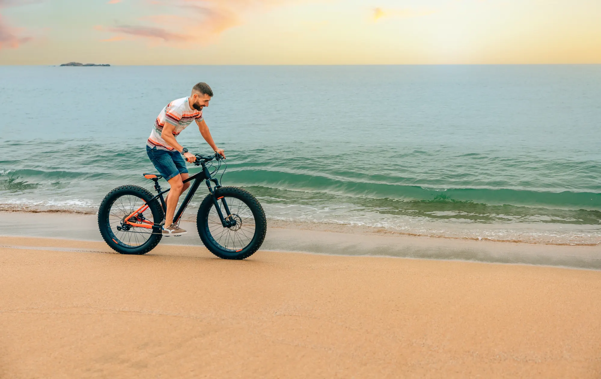 Ciclista pedalando uma fat bike na beira da praia