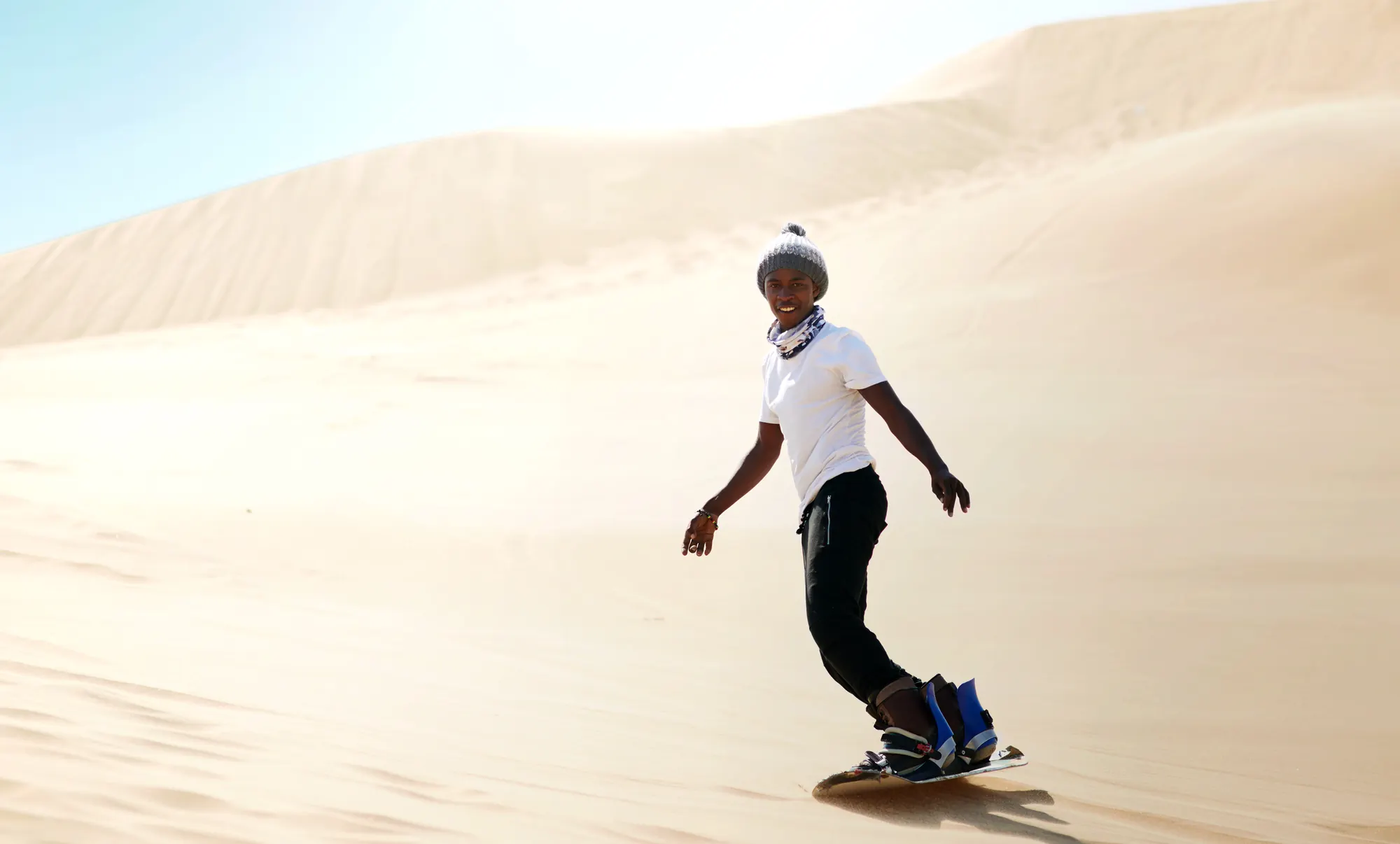 Pessoa descendo uma duna de areia clara em uma prancha de sandboard